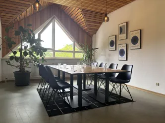 Ein moderner Besprechungsraum mit einem großen Tisch und schwarzen Stühlen. Große Fenster sorgen für viel Tageslicht und es gibt einige Pflanzen im Raum.