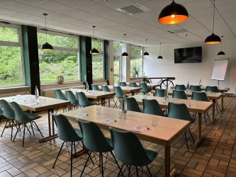 Ein moderner Konferenzraum mit Tischen und Stühlen. Große Fenster sorgen für viel Tageslicht und einen Blick ins Grüne.