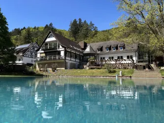 Ein gemütliches Hotelgebäude am Wasser, umgeben von Bäumen. Der Himmel ist klar und blau, was eine idyllische Atmosphäre schafft.