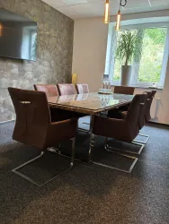 Ein modernes Besprechungszimmer mit einem großen Tisch und bequemen Stühlen. Durch ein Fenster kommt Tageslicht herein, und eine Pflanze sorgt für eine angenehme Atmosphäre.