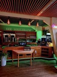 Eine moderne Bar mit Holzinterieur und grüner Beleuchtung. An der Bar stehen verschiedene Getränke und Gläser bereit.