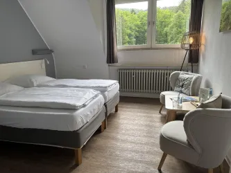 Ein gemütliches Hotelzimmer mit zwei einzelnen Betten. Das Zimmer ist hell und hat einen Blick auf das grüne Umland.