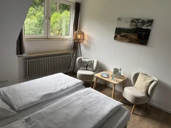Ein helles Schlafzimmer mit zwei Einzelbetten und einem gemütlichen Sitzbereich. Durch das Fenster hat man einen schönen Blick ins Grüne.