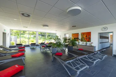 Ein modernes Ruhe- und Entspannungszimmer mit Liegen und Pflanzen. Große Fenster lassen viel Licht herein und bieten einen Blick ins Freie.