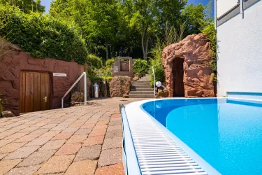 Ein schöner Außenbereich mit einem Pool und Steinwegen. Über dem Pool sieht man grünes Laub und eine entspannende Atmosphäre.