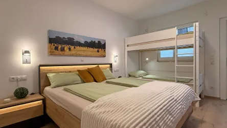 Ein modernes Schlafzimmer mit einem Doppelbett und einem Etagenbett. Die Wände sind in hellen Farben gestrichen und es gibt dekorative Elemente wie ein Bild und Pflanzen.
