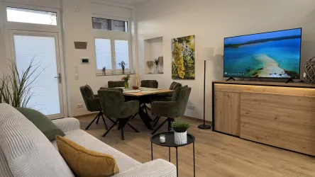 Ein gemütlicher Wohnbereich mit einem Fernseher und einem Esstisch. Die Möbel sind modern und in neutralen Farben gestaltet.