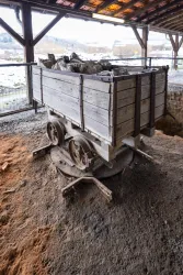Eine alte Holzkohlewagen auf Schienen. Er steht auf einem schmutzigen Boden in einer überdachten Umgebung.