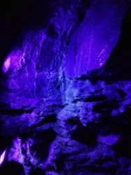 Eine faszinierende Felswand, beleuchtet in lila Tönen. Die Textur der Gesteine ist gut sichtbar und strahlt eine mysteriöse Atmosphäre aus.