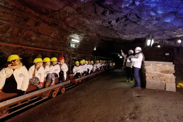 Eine Gruppe von Menschen sitzt in einem Bergwerk auf einer Lorenbahn. Die Teilnehmer tragen gelbe Helme und folgen einem Führer.
