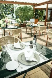 Ein elegantes Restaurant mit gedeckten Tischen im Freien. Die Tische sind mit Servietten und Gläsern dekoriert, umgeben von grünen Pflanzen.