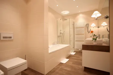 Ein modernes Badezimmer mit einer Badewanne und einer separaten Dusche. Es gibt eine elegante Waschtisch mit einem kleinen Blumenarrangement und helle Beleuchtung.