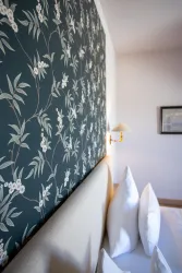 Ein gemütliches Schlafzimmer mit einer stilvollen Tapete und einem großen Bett. Die Wand ist mit einem botanischen Muster in sanften Farben dekoriert.