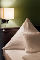 Ein gemütliches Schlafzimmer mit einem hellen Kissen und einer modernen Wandlampe. Die Wände sind in sanftem Grün gehalten.