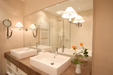 Ein modernes Badezimmer mit zwei Waschbecken und einem großen Spiegel. Es gibt eine Dusche und frische Blumen auf dem Tisch.