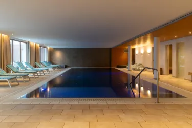 Ein eleganter Innenpool mit einer entspannenden Atmosphäre. Umgeben von bequemen Liegen und sanftem Licht.