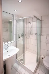 Ein modernes Badezimmer mit einer Glasdusche und weißen Fliesen. Das Waschbecken und die Toilette sind ebenfalls gut angeordnet.