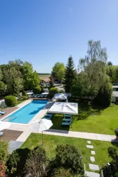 Ein schöner Garten mit einem Pool in der Mitte und vielen Bäumen. Sonnenschirme und Liegen laden zum Entspannen ein.