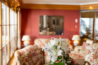 Ein gemütliches Wohnzimmer mit floralem Design und hellen Farben. Im Vordergrund stehen Blumenarrangements, während ein Spiegel die Wand ziert.