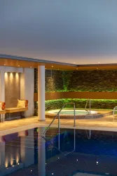 Ein eleganter Wellnessbereich mit einem Pool und einem Whirlpool. Die Beleuchtung und die Steinwände schaffen eine entspannende Atmosphäre.