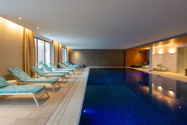 Ein eleganter Innenpool mit blauen Liegen und großen Fenstern. Das Ambiente ist entspannt und einladend.