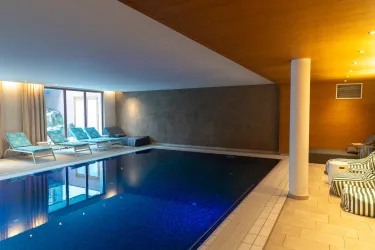 Ein eleganter Innenpool mit bläulichem Wasser und gemütlichen Liegen. Das Ambiente ist modern und einladend, mit sanften Lichtakzenten.