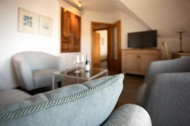 Ein moderner Wohnraum mit gemütlichen Sesseln und einem kleinen Tisch. Im Hintergrund sind ein Fernseher und eine Holzkommode sichtbar.