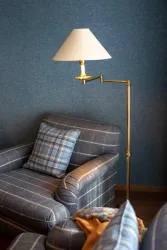 Ein gemütlicher Wohnbereich mit einem blauen Wandschmuck und einem bequemen Sessel. Eine elegante Stehlampe aus Messing beleuchtet den Raum.