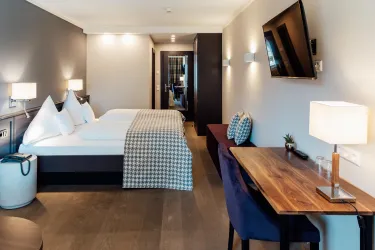 Ein modernes Hotelzimmer mit zwei Betten, einem Tisch und eleganter Beleuchtung. Die Wände sind neutral gestrichen und es gibt eine gemütliche Atmosphäre.