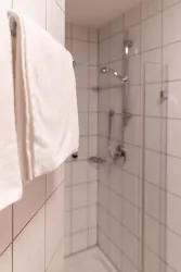Ein modernes Badezimmer mit einer Dusche und weißen Handtüchern. Die Wände sind mit hellen Fliesen gefliest.