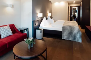 Ein modernes Zimmer mit zwei Betten und einem roten Sofa. Die Einrichtung ist minimalistisch und stilvoll, ideal für einen komfortablen Aufenthalt.