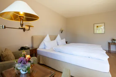 Ein gemütliches Schlafzimmer mit einem großen Bett und weißen Bettwäsche. Es gibt einen kleinen Tisch mit Blumen und eine angenehme Lichtquelle.