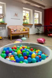 Ein bunter Ballpool mit vielen kleinen Bällen in verschiedenen Farben. Im Hintergrund sind ein Sofa und einige Spielzeuge zu sehen.