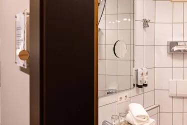 Ein modernes Badezimmer mit gefliesten Wänden. Im Hintergrund sind Handtücher und Toilettenartikel zu sehen.