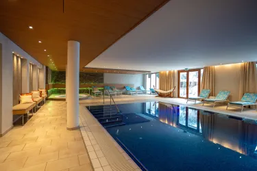 Ein eleganter Schwimmbereich mit klarem Wasser und modernen Liegen. Große Fenster lassen viel Licht herein und schaffen eine entspannte Atmosphäre.