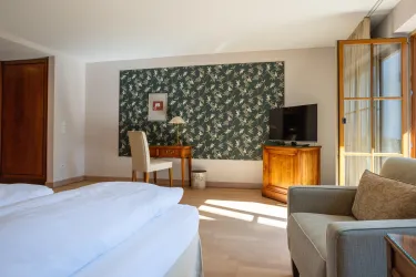 Ein gemütliches Hotelzimmer mit einem Doppelbett und einem Schreibtisch. Die Wände sind mit einem schönen, floralem Muster dekoriert.