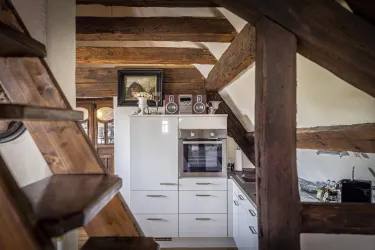 Eine moderne Küche mit weißen Möbeln und Holzbeamten. Im Hintergrund sind Treppen und dekorative Elemente zu sehen.