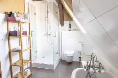 Ein modernes Badezimmer mit einer Glasdusche, WC und einer Badewanne. Regale mit Handtüchern und Pflegeprodukten ergänzen die Einrichtung.