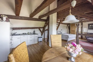 Eine helle, gemütliche Wohnung mit Holzbalken und modernem Mobiliar. Der Wohnbereich ist offen und einladend, mit einer kleinen Küchenecke und einem Esstisch.