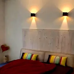 Ein gemütliches Schlafzimmer mit einem großen Bett und bunten Kissen. An den Wänden leuchten zwei moderne Wandlampen.