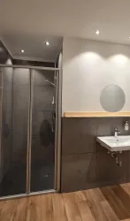 Ein modernes Badezimmer mit einer Dusche und einem Waschbecken. Die Wände sind neutral gefärbt und der Boden ist aus Holz.