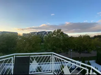 Eine Aussicht von einem Balkon mit einer grünen Landschaft und Bäumen. Der Himmel ist leicht bewölkt und es wird spät nachmittags.