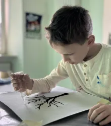 Ein Junge malt konzentriert einen Baum auf ein Blatt Papier. Er verwendet eine Pipette, um die Farbe präzise aufzutragen.