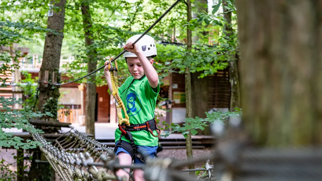 Junge klettert über Hängebrücke im Kletterpark