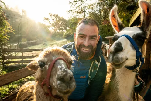 Mann lächelt mit zwei Lamas in die Kamera