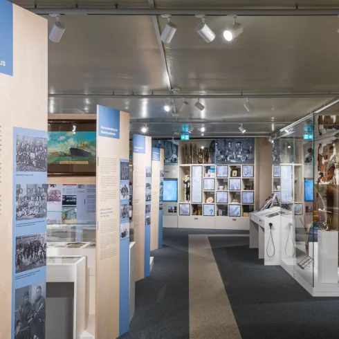 Ein Museum mit Ausstellungswänden und historischen Fotografien. Im Raum sind verschiedene Exponate und Informationsstände zu sehen.